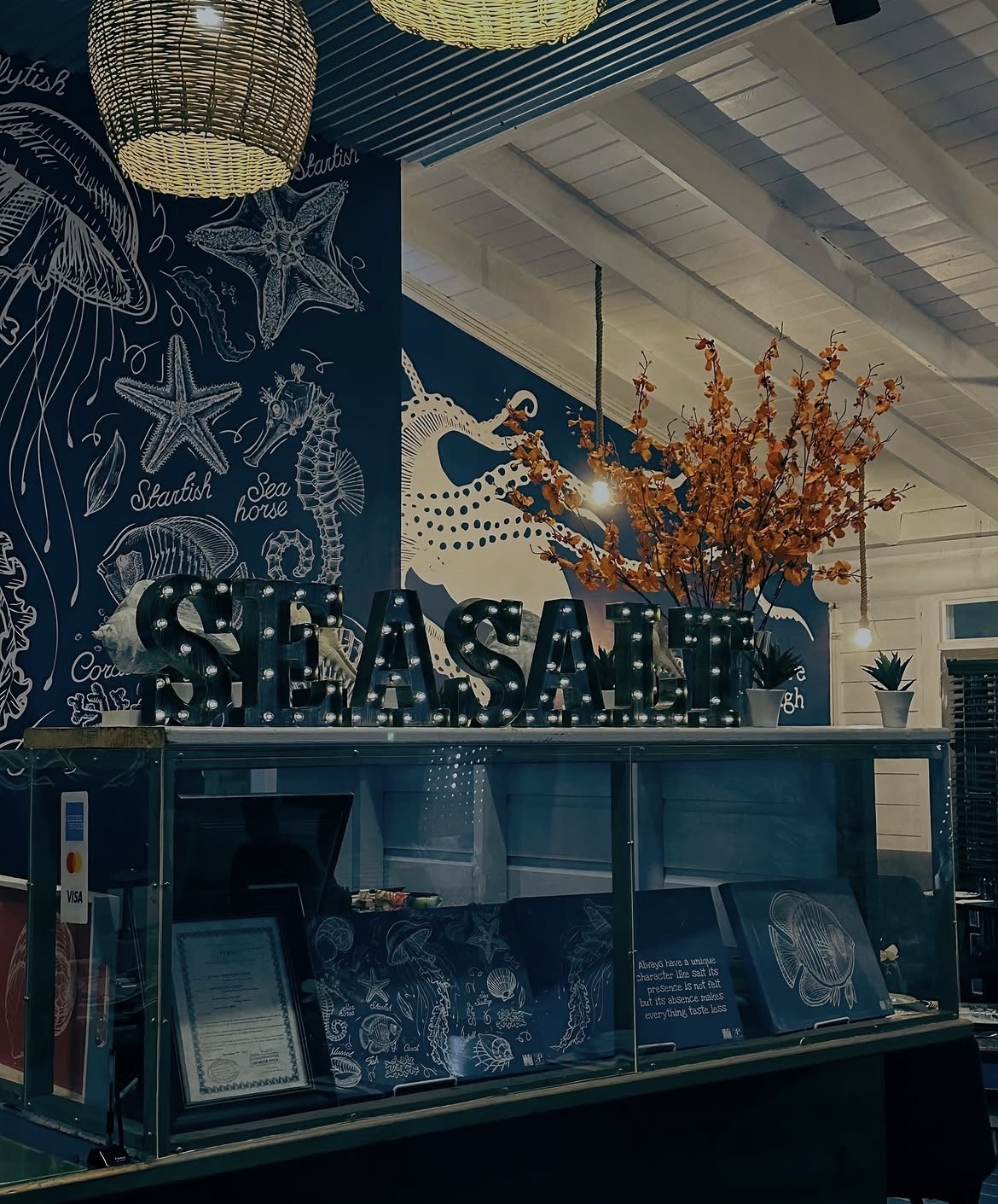Lit SEA SALT marquee letters against the hand-drawn sea life mural