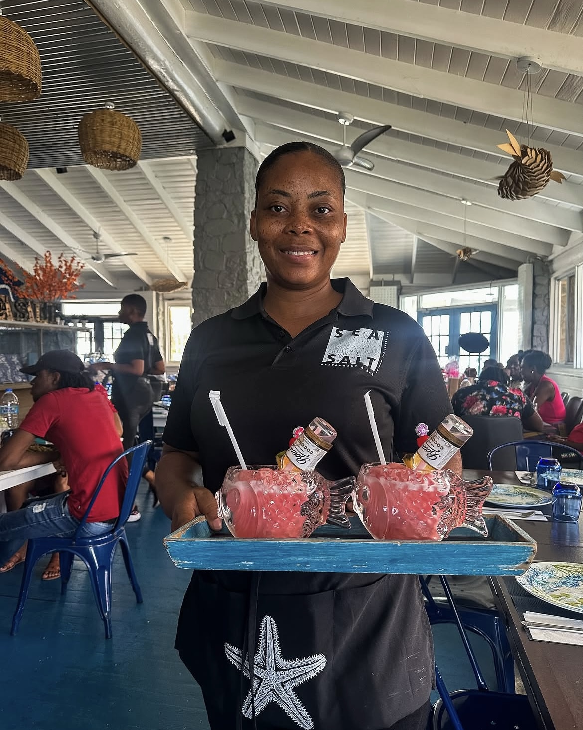 Sea Salt server carrying a tray of pink cocktails in fish-shaped glasses