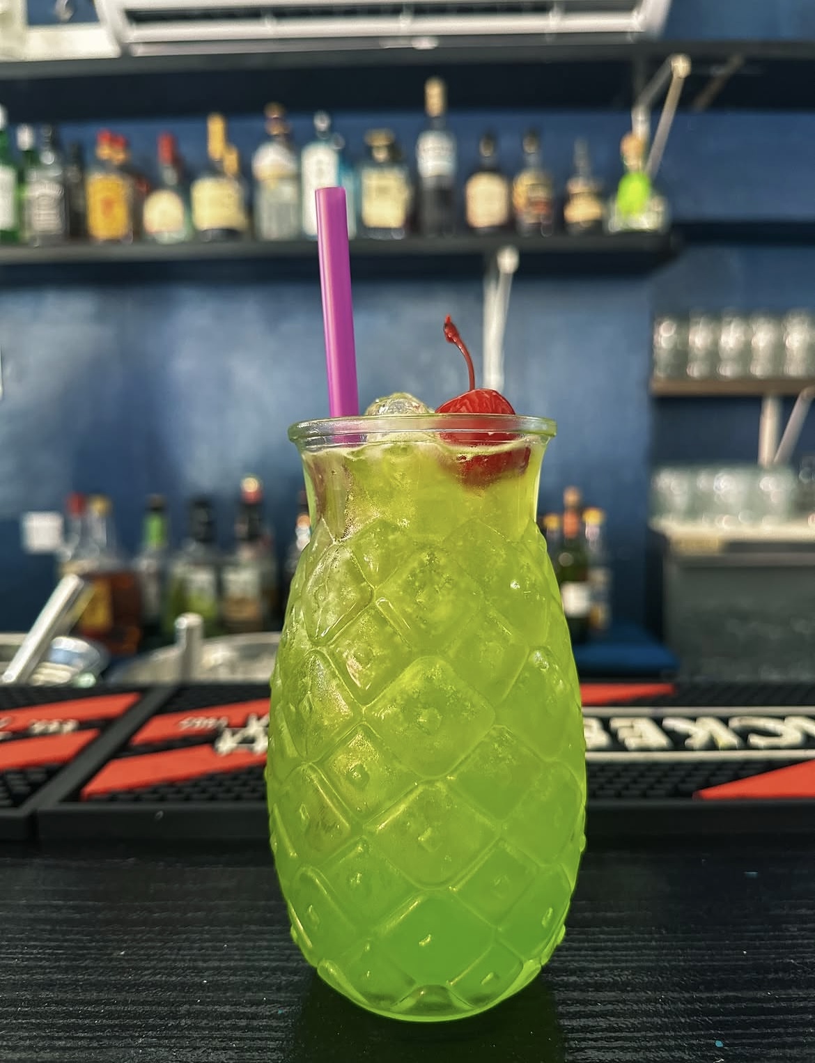 Bright green cocktail in a pineapple glass at the bar