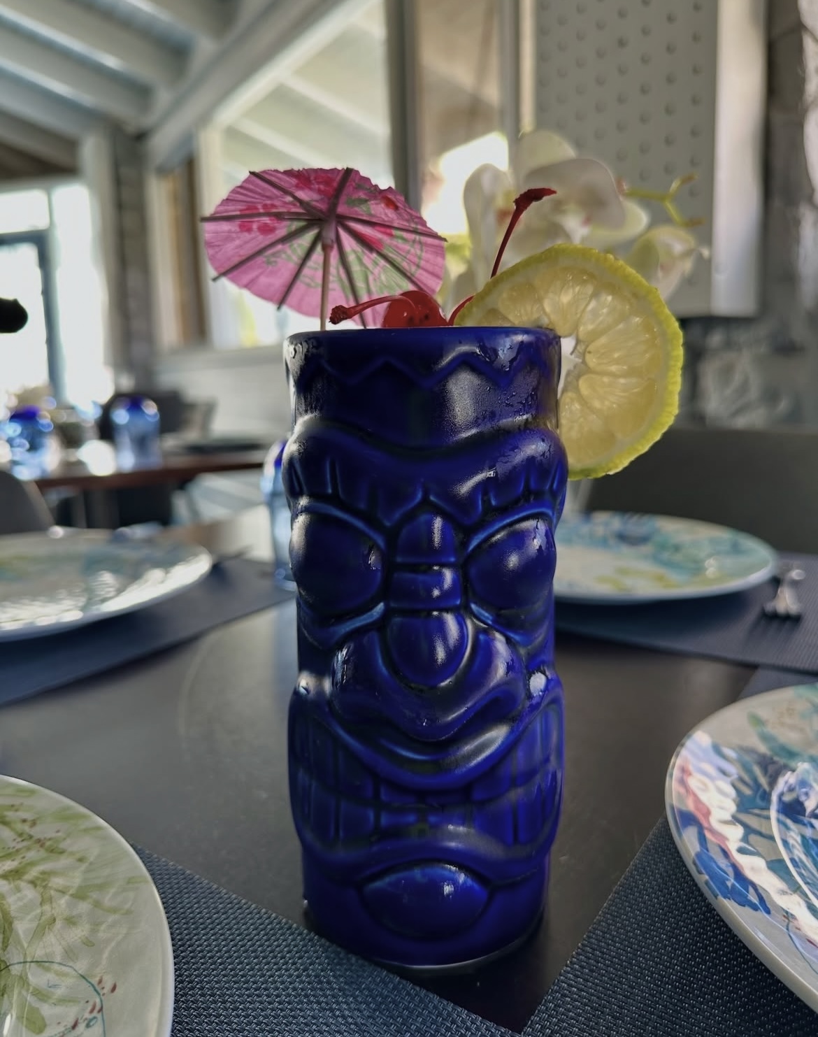 Cocktail in a cobalt blue tiki mug with a paper umbrella